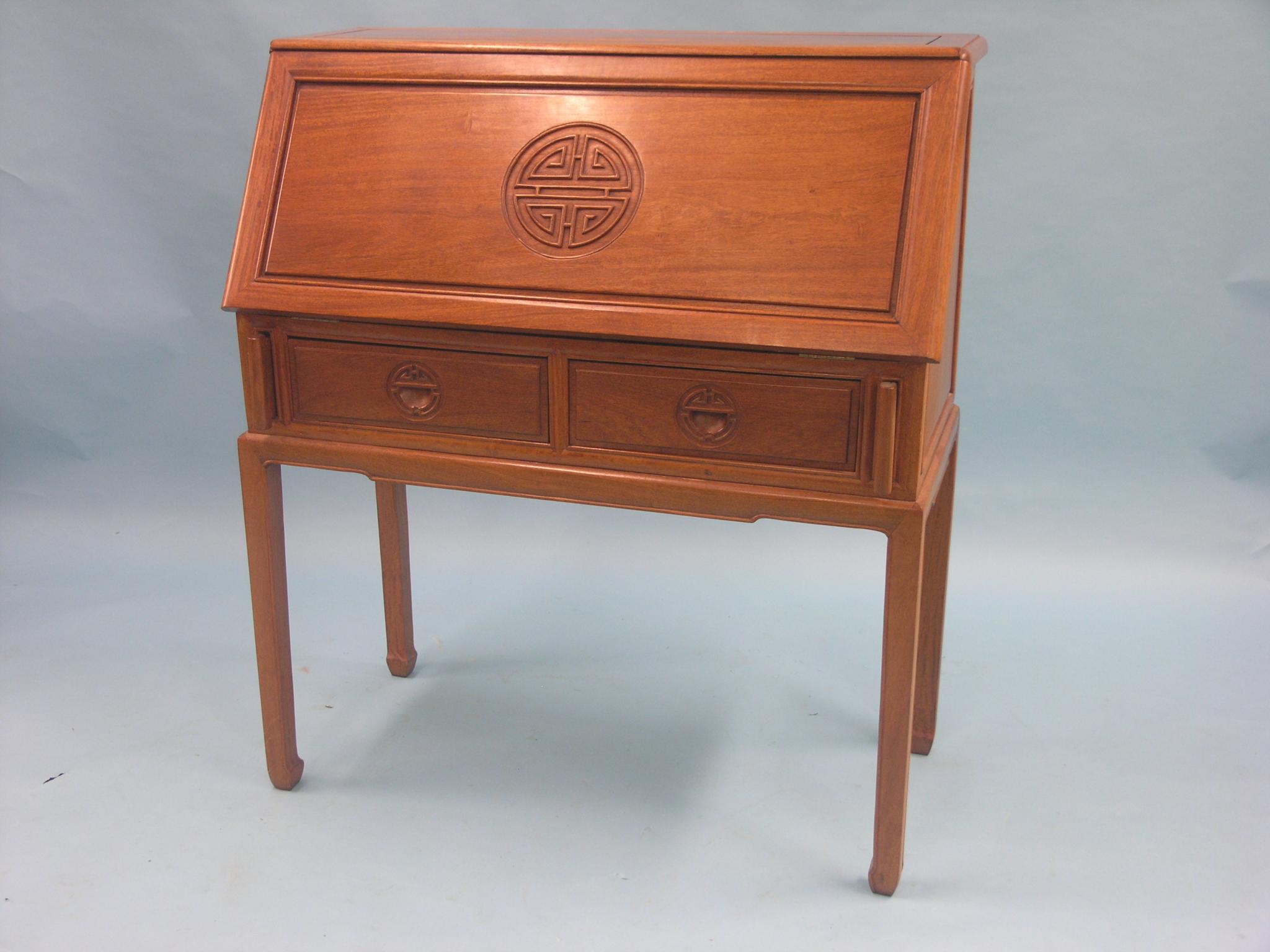 An Eastern hardwood bureau, fall-front with carved medallion, enclosed fittings above two drawers,