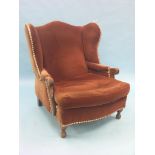 An oak-framed wing armchair, upholstered in a buttoned rust dralon