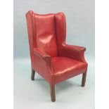 An early 20th century mahogany-framed wing armchair, upholstered in a claret leather, on moulded