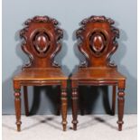 A pair of Victorian mahogany hall chairs with shaped and fretted backs, with scroll carving, wood