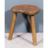 A mid-20th Century oak three legged stool by Thompson of Kilburn, the shaped seat carved with a