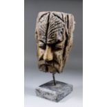 A modern driftwood carving of a moustachioed male head with furrowed brow, on black painted wood