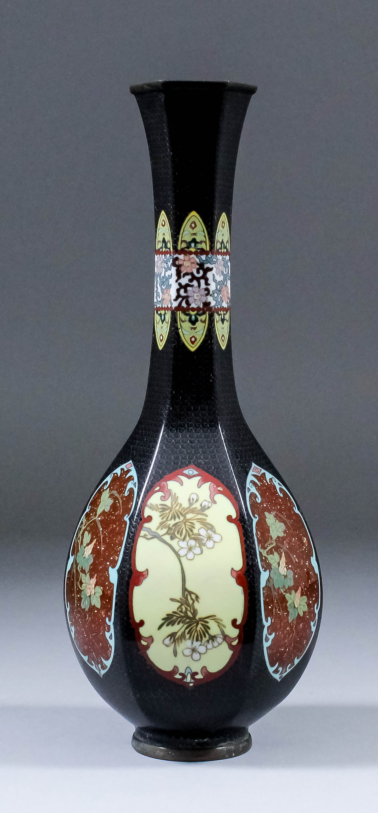 A Japanese cloisonne bottle vase of panelled form, the sides with flowering branches within shaped