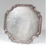 A George V silver square salver with shaped and moulded rim and re-entrant corners, the centre