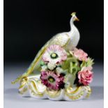 A Royal Crown Derby bone china figure of a peacock standing amidst naturalistically modelled