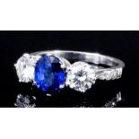 A modern silvery coloured metal mounted sapphire and diamond three stone ring, the central oval