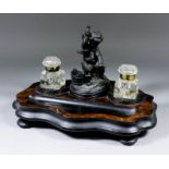 A Continental walnut and ebonised ink stand with a spelter figure of "Cupid at Vulcan's Forge", on