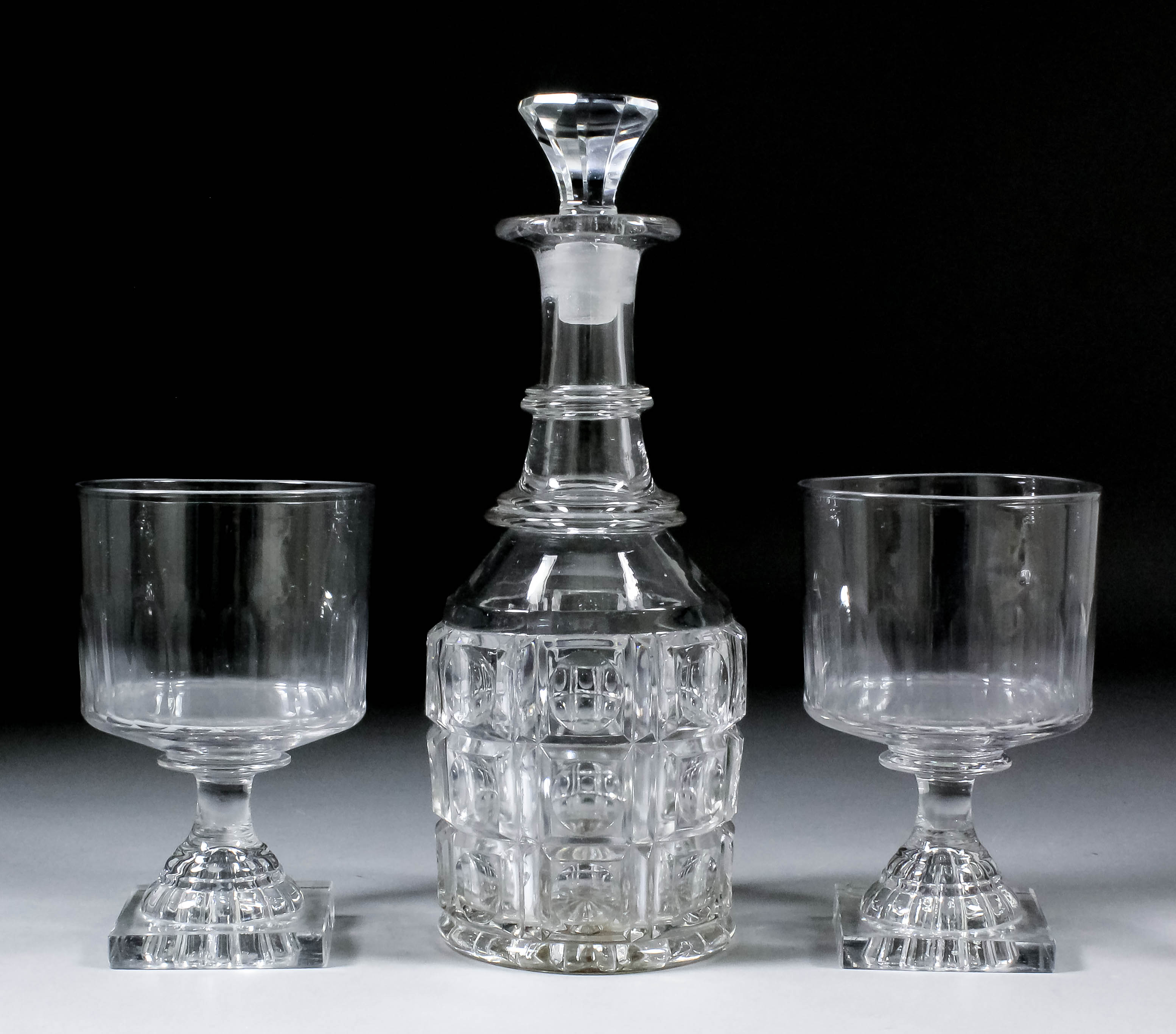 A pair of early 19th Century straight-sided and panel cut glasses, on square lemon squeezer feet,