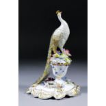 A Royal Crown Derby bone china figure of a peacock standing on a flower encrusted urn, 9.75ins high,