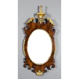 A mahogany framed and parcel gilt oval wall mirror, with bow front reeded and bellflower cresting,