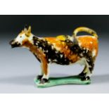 A 19th Century English pottery cow creamer, sponged in orange and brown, on a shaped flat base, 4.