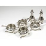 A George V silver six piece condiment set with moulded rims and on scroll supports with hoof pattern