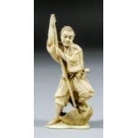 A Japanese carved and stained ivory okimono of a hunter slaying an eagle, his left foot raised on