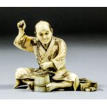 A Japanese carved and stained ivory okimono of a seated barrel maker, his right hand raised (now