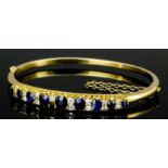 A late 19th Century 15ct gold sapphire and diamond set stiff bangle, the face set with nine oval cut