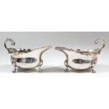 A pair of George VI silver oval sauce boats with shaped rims, high leaf capped scroll handles, on