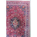 A Meshed carpet woven in colours with a bold central medallion filled with floral motifs and