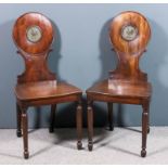 A pair of George III mahogany hall chairs, the circular backs painted with a crest, wood seats,