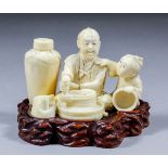 A Japanese carved sectional ivory Okimono of a seated worker milling or grindings, with a young