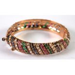 GOLD COLOURED METAL HINGE OPENING BANGLE, with spiral rows set with emeralds, rubies, diamonds,