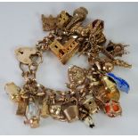 9ct GOLD CURB PATTERN CHARM BRACELET, with hallmarked solid links, padlock clasp and twenty six gold