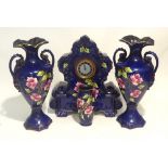 AN EDWARDIAN POTTERY CLOCK GARNITURE IN BLUE WITH FLORAL AND GILT DECORATION AND A MATCHING SMALL