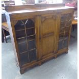 AN OAK DWARF BOOKCASE WITH CENTRE PANEL, FOLDING DOOR FLANKED BY TWO PANE PANEL GLAZED DOORS, ON