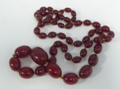 A CONTINUOUS LONG SINGLE STRAND NECKLACE of opaque dark red amber graduated beads, strung on a