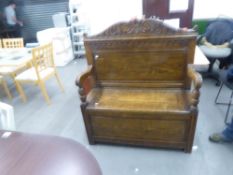 AN EDWARDIAN OAK SETTLE, SHAPED BACK, REEDED ARMS WITH SCROLL ENDS, HINGE LID TO THE SEAT, ALL
