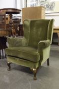 A WINGED FIRESIDE ARMCHAIR COVERED IN GREY/GREEN VELVET, ON CABRIOLE FRONT SUPPORTS