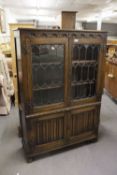 A CARVED OAK DISPLAY CABINET WITH LEADED AND GLAZED DOORS AND LINENFOLD DECORATION