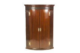 GEORGE III MAHOGANY BOW FRONTED HANGING CORNER CUPBOARD, with cavetto cornice over a blind fret