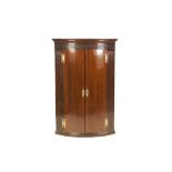 GEORGE III MAHOGANY BOW FRONTED HANGING CORNER CUPBOARD, with cavetto cornice over a blind fret