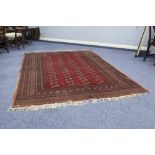 PAKISTAN BOKHARA CARPET WITH FOUR ROWS OF GULS on a crimson field, the broad borders having multiple