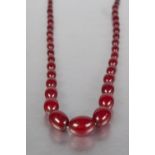 A NECKLACE OF DARK RED AMBER GRADUATED OVAL BEADS, approx 30" long