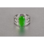 CHINESE WHITE GOLD COLOURED METAL BROAD RING, set with a rounded oblong green jade, the broad