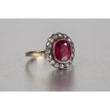 A LATE VICTORIAN/EDWARDIAN 18ct GOLD RING, set with a ruby coloured stone within a surround of