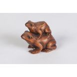 A JAPANESE WELL CARVED BOXWOOD NETSUKE of a small frog on the back of a larger frog, with glass