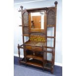 AN EDWARDIAN OAK HALLSTAND WITH BEVELLED RECTANGULAR MIRROR SURROUNDED BY PANELS OF BRONZED EMBOSSED