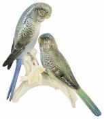 A Karl Ens porcelain figurine of Budgies each perched on a tree trunk, factory marks to base and