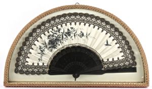 An Edwardian ladies fan in a demi-lune display case the cream satin painted in black with floral