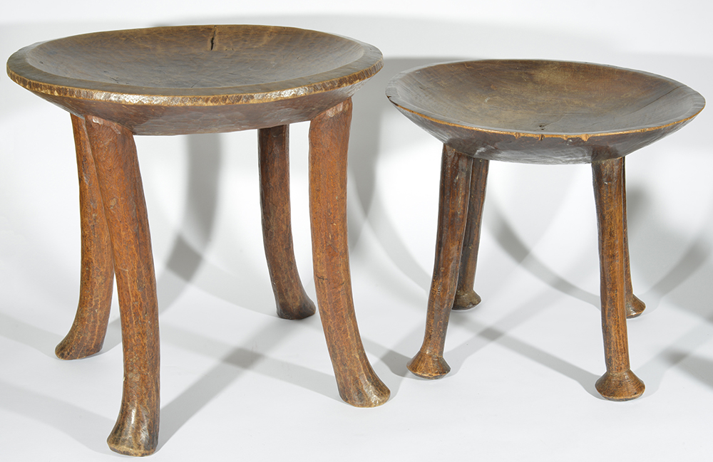 Two 20th century African tribal stools, each with dished seats upon four supports, together with a