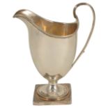 A George III silver cream jug, London 1790 of helmet form with ribbed handle upon a square