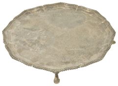A George V silver salver, London 1928 the shaped border with gadrooned edge, raised upon three pad