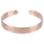 An early 20th century scroll engraved open banglethe rose coloured metal with floral and scroll