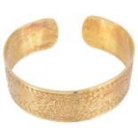 A wide Continental yellow metal engraved cuff bangledecorated with flower posies on a plannished