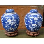 PAIR OF ORIENTAL STYLE BLUE AND WHITE PRUNUS PATTERN STORAGE JARS WITH COVERS ON WOODEN STANDS