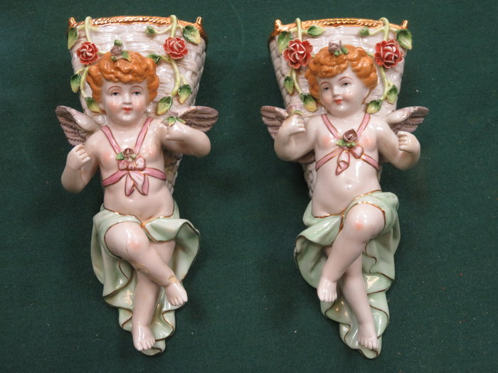 PAIR OF CONTINENTAL HANDPAINTED AND GILDED RELIEF DECORATED CHERUB FORM WALL POCKETS (AT FAULT)