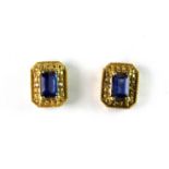 A pair of yellow metal stud earrings set with emerald cut sapphires, L. 1cm (one sapphire a/f).