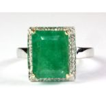 A 9ct white gold ring set with an emerald cut emerald surrounded by diamonds, (O).